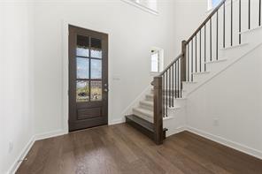 Entryway featuring dark-toned wood-finish flooring, a multi-pane glass-panel front door, and a staircase with stained wood newel posts and dark metal balusters