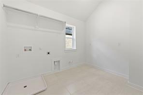 Laundry room featuring vaulted ceilings, neutral tile flooring, built-in wall shelving, and a singular window