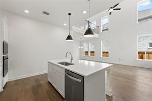 Kitchen featuring an island with a stone countertop, an undermount stainless steel sink, built-in stainless steel appliances, wood-finish flooring, and pendant lighting