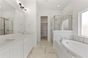 Bathroom featuring a dual-sink vanity with white cabinetry, quartz-style countertops, an enclosed glass-paneled shower, and a soaking tub