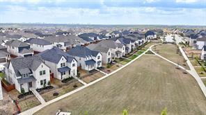 Aerial perspective of a residential development featuring single-family dwellings with multi-pitch roofs, masonry exteriors, concrete walkways, and an expansive common green space
