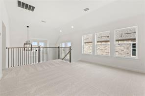 Open-concept space featuring vaulted ceilings, neutral wall-to-wall carpeting, metal spindle railing, and a geometric pendant light fixture