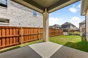 Covered concrete patio featuring a masonry-clad support pillar, wooden privacy fencing, and a sodded lawn