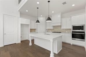 Kitchen featuring white shaker-style cabinetry, center island with stone-finish countertop, dual stainless steel wall ovens, recessed lighting, and wood-finish flooring