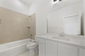 Bathroom featuring a white vanity with a composite countertop, an integrated rectangular sink, a large wall-mounted mirror, and a tiled shower-tub surround with a built-in shelf
