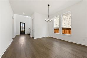 Open-concept room featuring wide-plank wood-finish flooring, dual windows with stone veneer accents, and a tiered multi-light chandelier