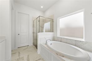 Soaking tub with chrome faucet, glass-enclosed shower, stone-finish flooring, and large window with privacy glass