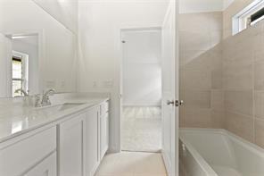 Bathroom featuring white cabinetry, quartz vanity countertop, integrated sink, chrome dual-handle faucet, and tile-surround bathtub