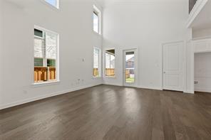 Two-story living area featuring vaulted ceilings, wood-finish flooring, multiple oversized windows, and a glass-paneled exterior door