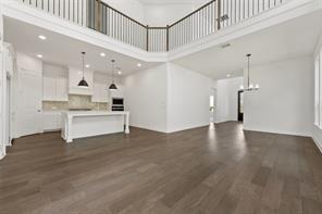 Open-concept floor plan featuring wood-finish flooring, two-story ceiling, mezzanine balcony with metal railing, and kitchen with central island and recessed lighting