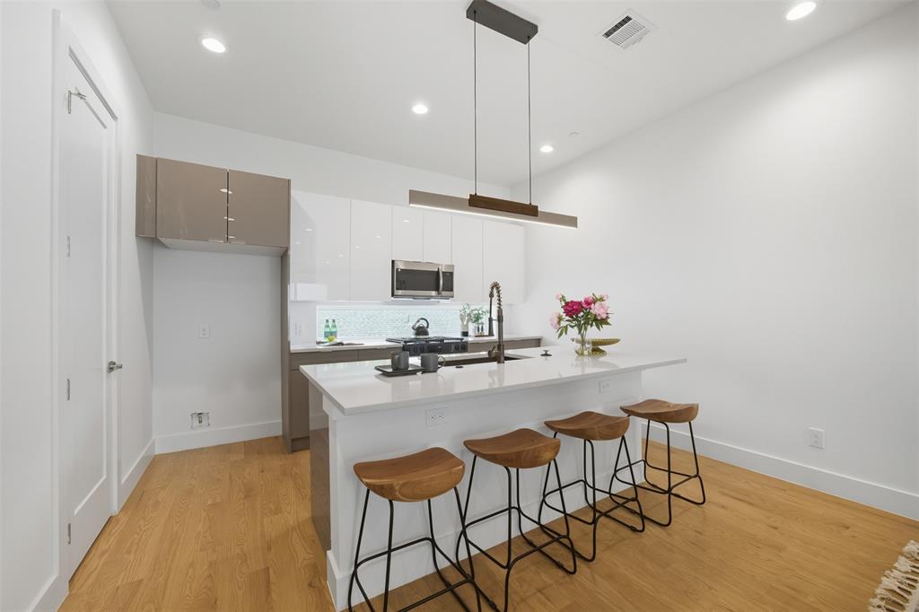 Kitchen featuring two-tone flat-panel cabinetry, quartz countertops, a geometric tile backsplash, stainless steel built-in microwave, and recessed lighting