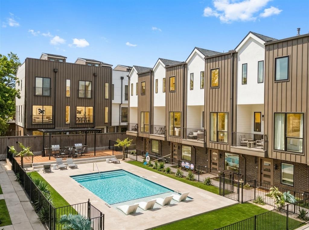 Multi-level architectural exterior featuring vertical metal siding, stucco finish, brick masonry, and private balconies with metal railings overlooking a community swimming pool and hardscaped patio area