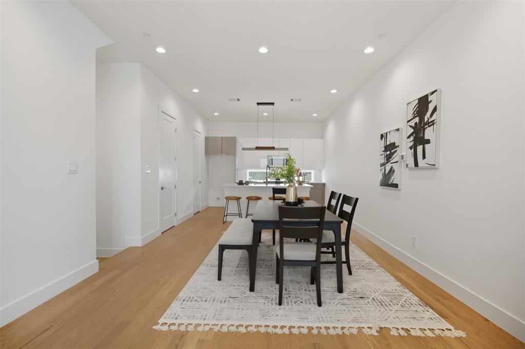 Open concept kitchen and dining area featuring wood-finish flooring, recessed lighting, white cabinetry, a center island with a stone-surface countertop, and a contemporary linear pendant light fixture