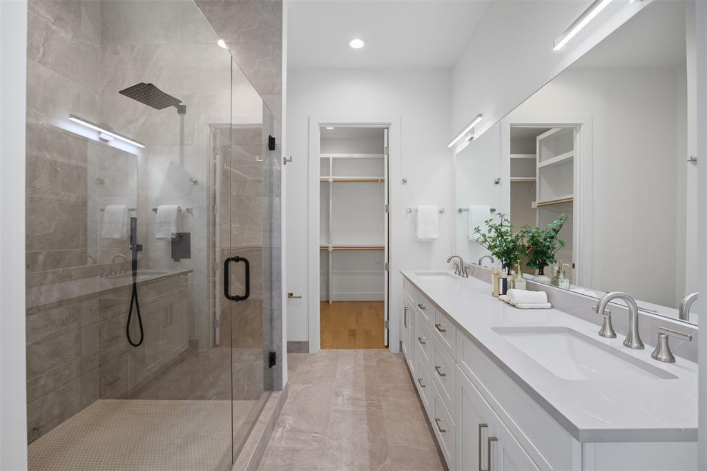 Dual-sink vanity with quartz countertops, glass-enclosed shower featuring large-format tile, wall-to-wall mirror, and recessed lighting