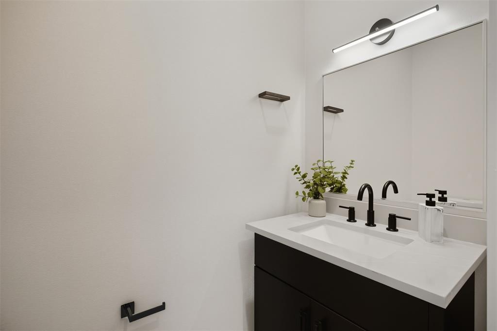 Dark vanity featuring a light-toned solid surface countertop with an integrated rectangular sink, matte black widespread faucet, framed wall-mounted mirror, and linear LED vanity light