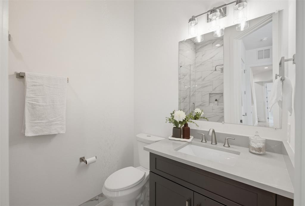 Bathroom featuring a dark wood-finish vanity, light-toned stone countertop, integrated rectangular sink, brushed-nickel faucet, and three-light wall-mounted fixture