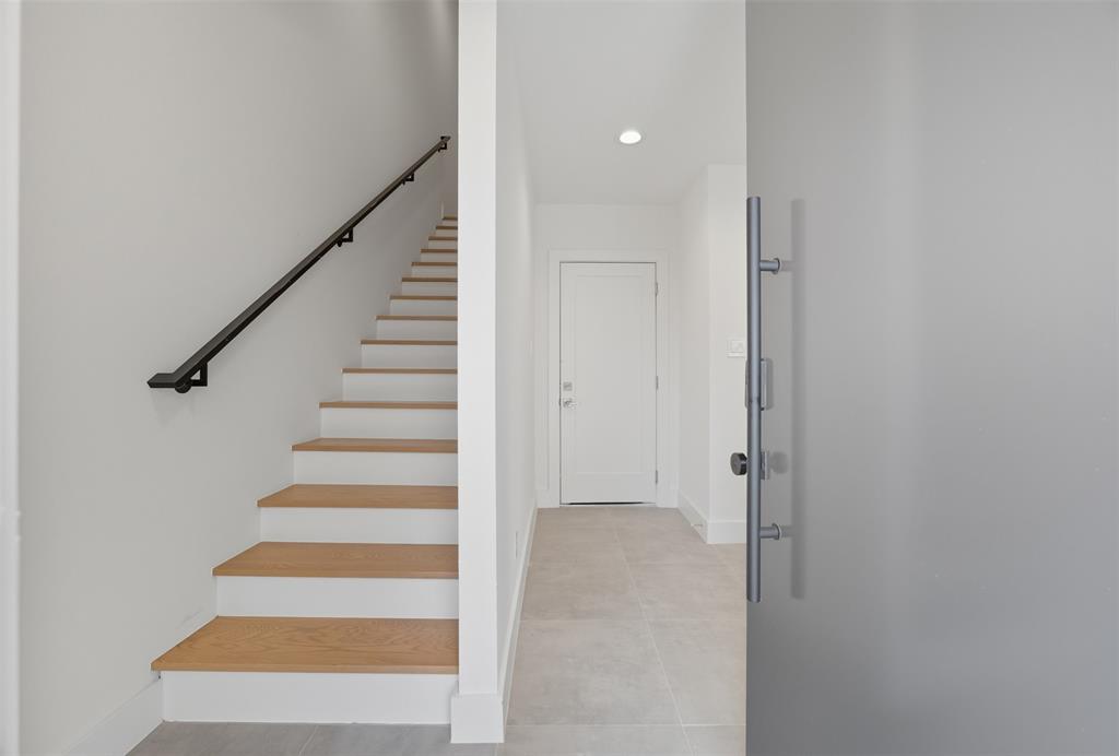 Entryway featuring a large frosted glass door with a stainless steel vertical pull handle, staircase with wood-finish treads, and a matte black handrail