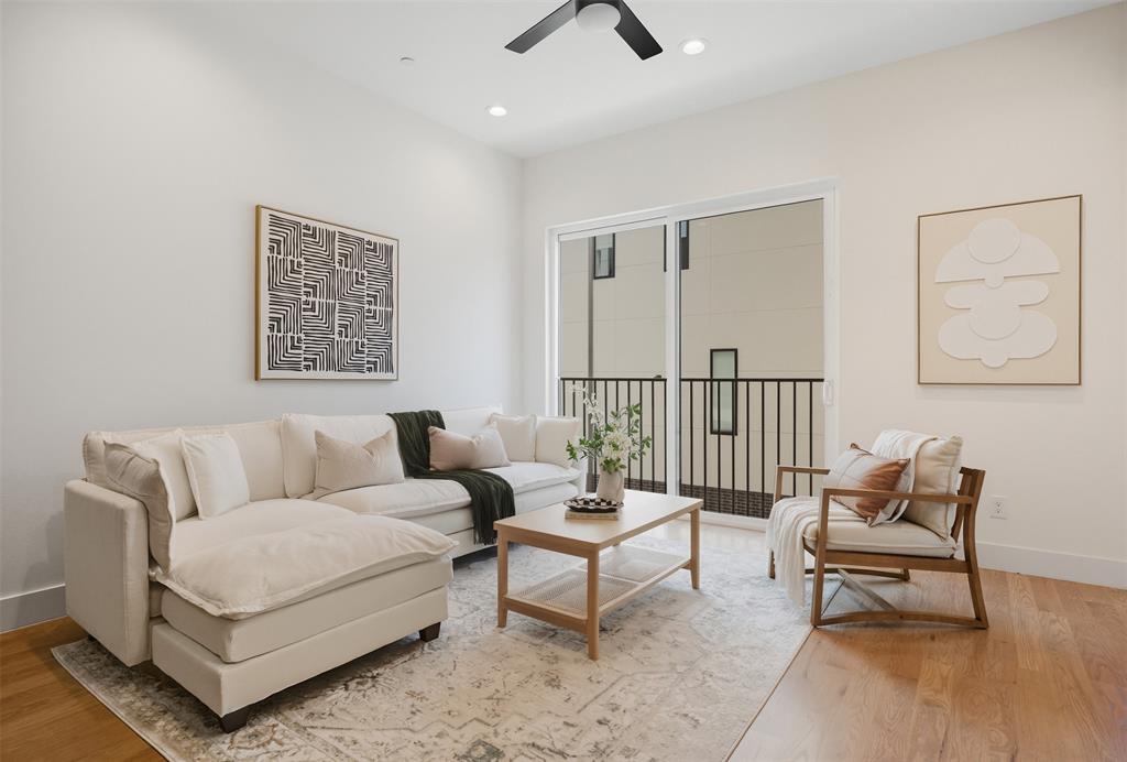 High-ceilinged room featuring wood-finish flooring, recessed lighting, a modern ceiling fan, and sliding glass doors with an exterior balcony
