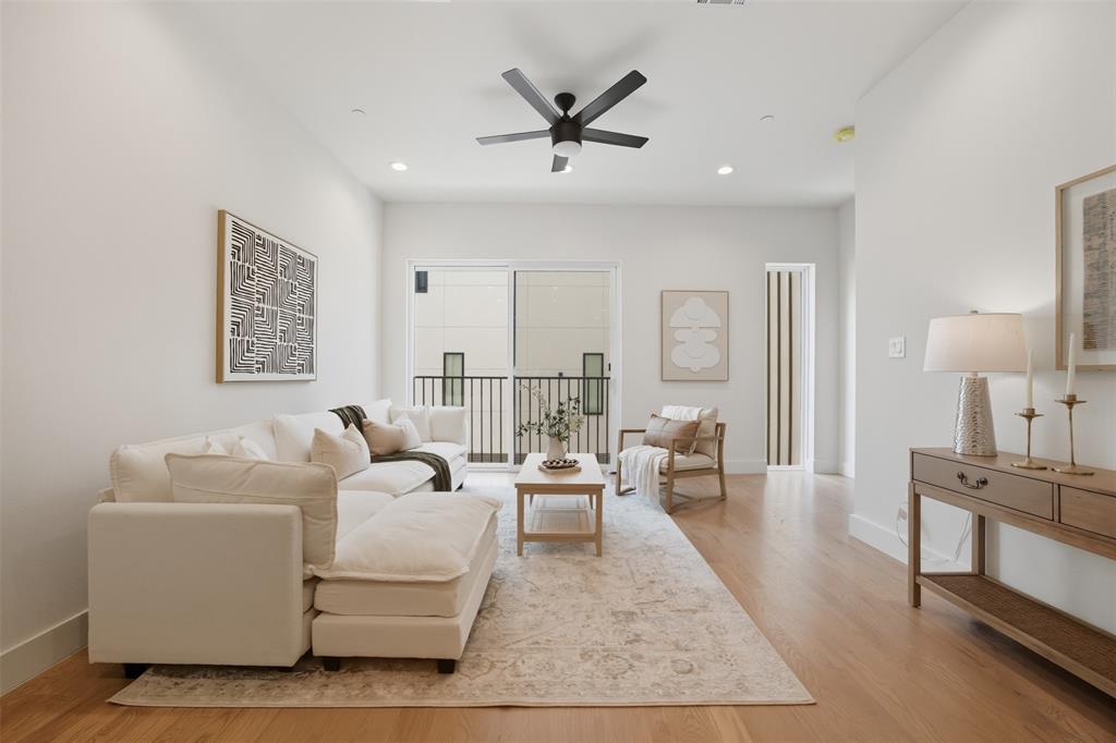 Living area featuring wood-finish flooring, recessed lighting, a matte black ceiling fan, and sliding glass doors with access to a balcony with metal railings