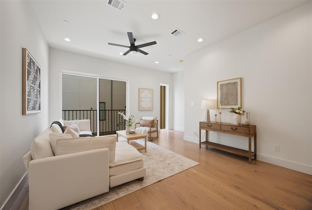 Living area featuring wood-finish flooring, recessed lighting, matte black ceiling fan, and sliding glass door with balcony access