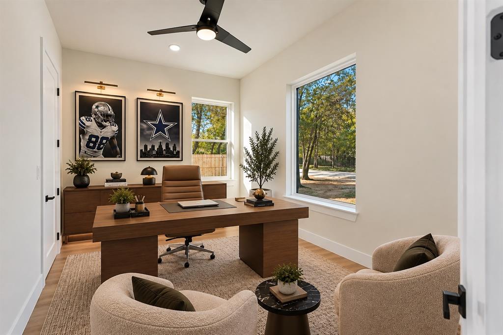 Neutral-toned room featuring wood-finish flooring, two large windows, a matte black ceiling fan with integrated lighting, and dual wall-mounted picture lights