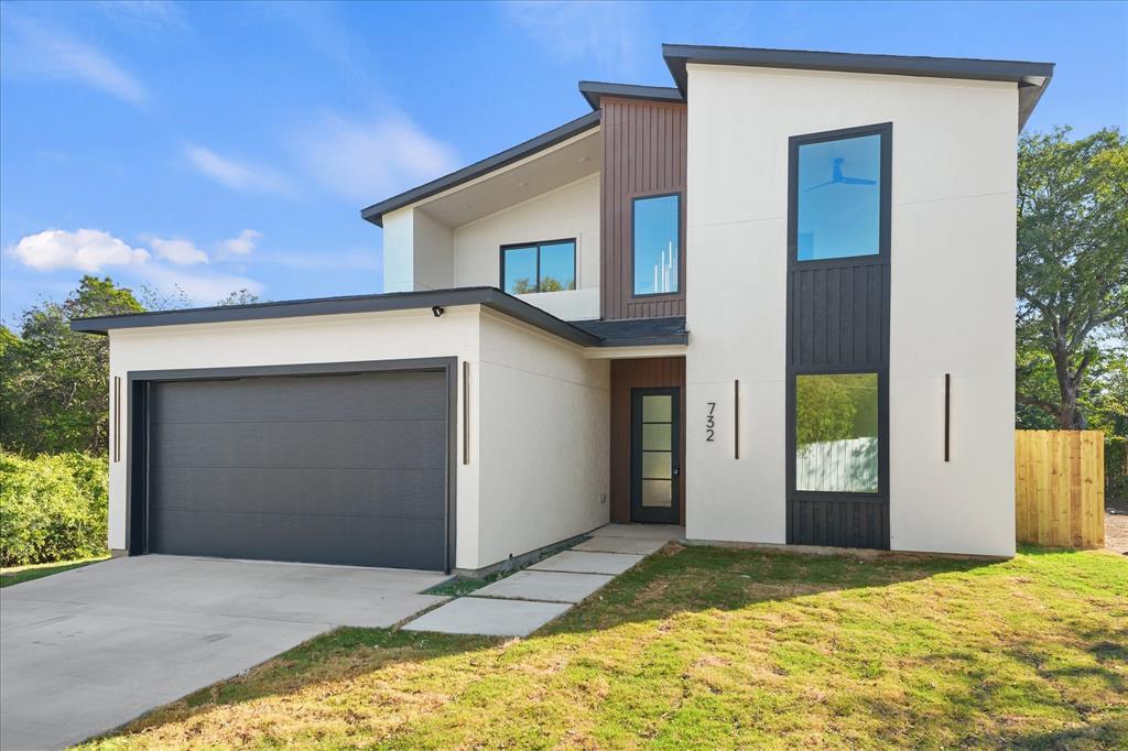 Contemporary two-story exterior featuring smooth stucco siding, vertical wood-tone accent paneling, large fixed-pane windows with black frames, and an attached two-car garage
