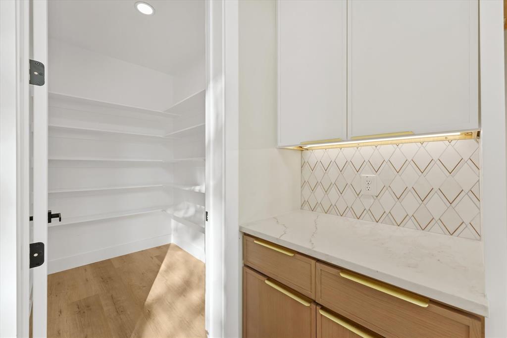 Custom cabinetry featuring light-toned wood base units, white upper cabinets, stone-composite countertops, geometric tile backsplash, and wood-finish flooring