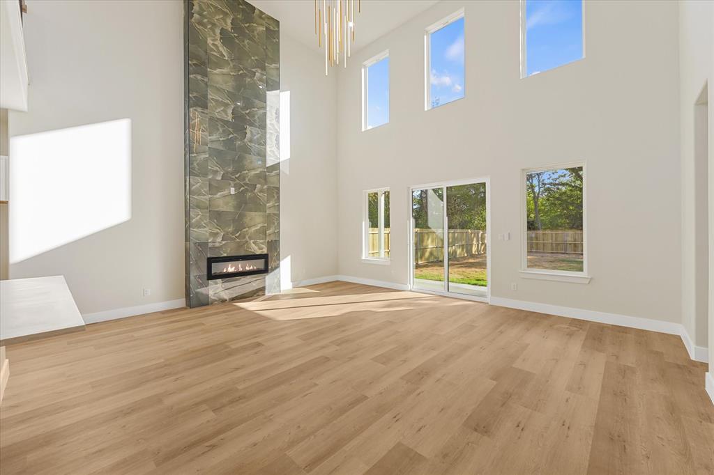 Double-height ceilings featuring large windows, floor-to-ceiling stone fireplace surround with built-in horizontal firebox, wood-finish flooring, and modern linear pendant lighting