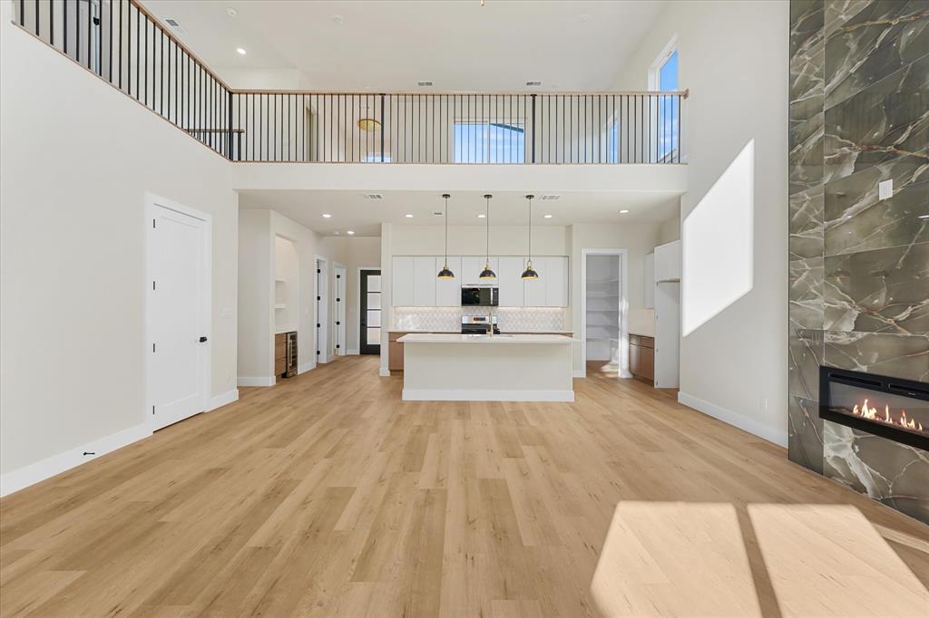 Double-height ceiling with a mezzanine overlook, full-height stone-clad linear fireplace, center island kitchen with pendant lighting, and light-toned wood-finish flooring