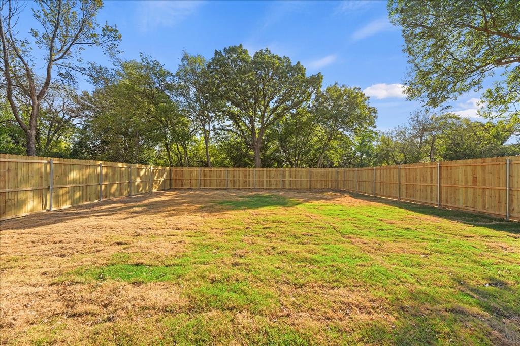 Expansive backyard featuring a wood-paneled perimeter fence, natural sod, and mature canopy trees