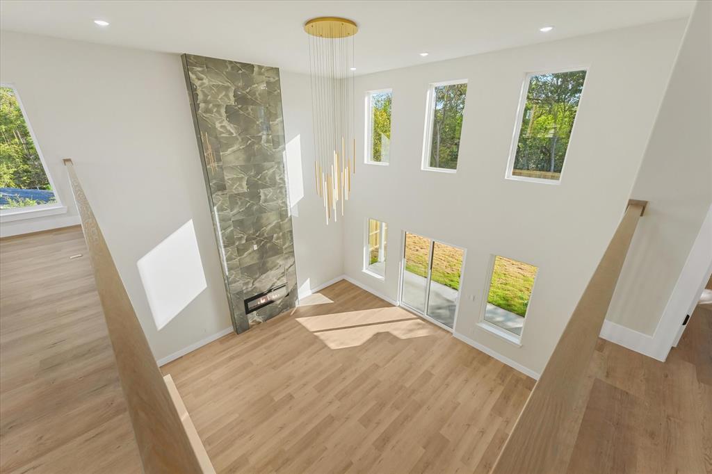 Double-height living area featuring a stone-clad floor-to-ceiling fireplace, wood-finish flooring, multi-level windows, and a suspended multi-light fixture