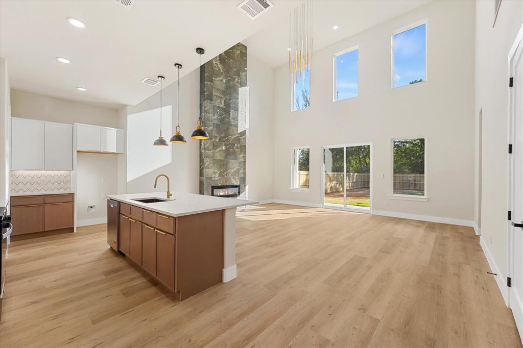 Kitchen featuring two-tone cabinetry, stone-finish countertops, herringbone-patterned tile backsplash, wood-finish flooring, and pendant lighting