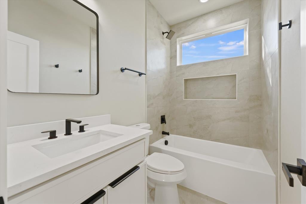 Bathroom featuring a white vanity with a solid-surface countertop, rectangular undermount sink, matte black hardware, and a tub-shower combination with tiled wall surround and recessed shelving