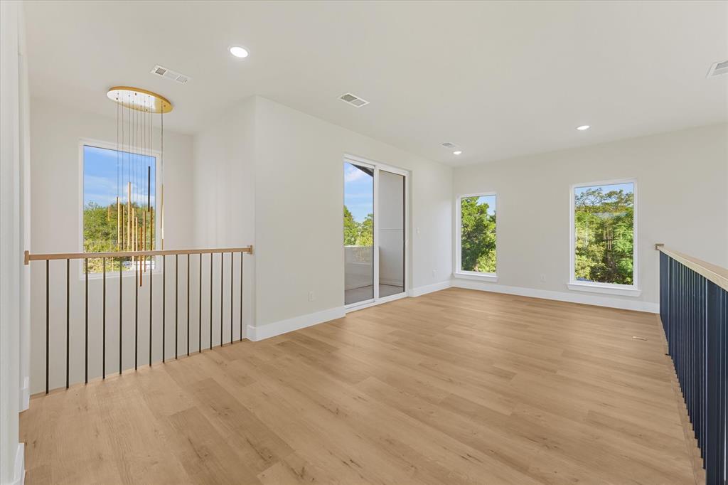 Open-concept space featuring wood-finish flooring, recessed lighting, expansive windows, a modern metal spindle railing, and sliding glass doors