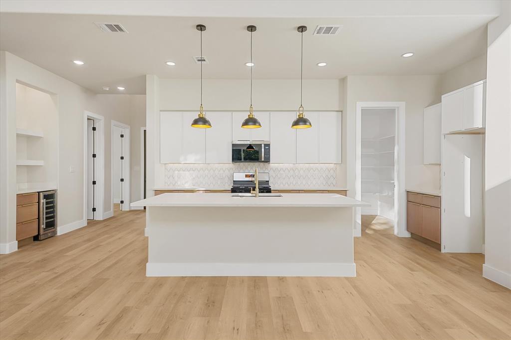 Kitchen featuring a central island with a quartz countertop, white flat-panel cabinetry, geometric pattern backsplash, three pendant lights, and built-in beverage refrigerator