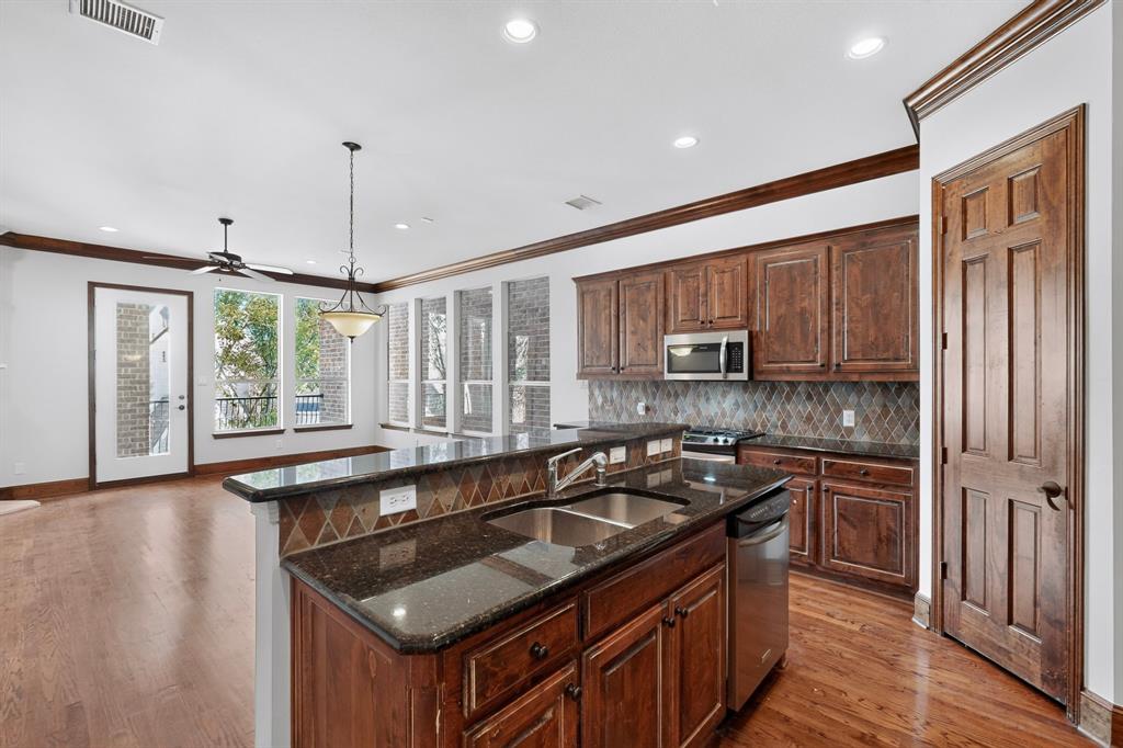 Kitchen featuring dark stone countertops, stained wood cabinetry, a tile backsplash, recessed lighting, and wood-finish flooring