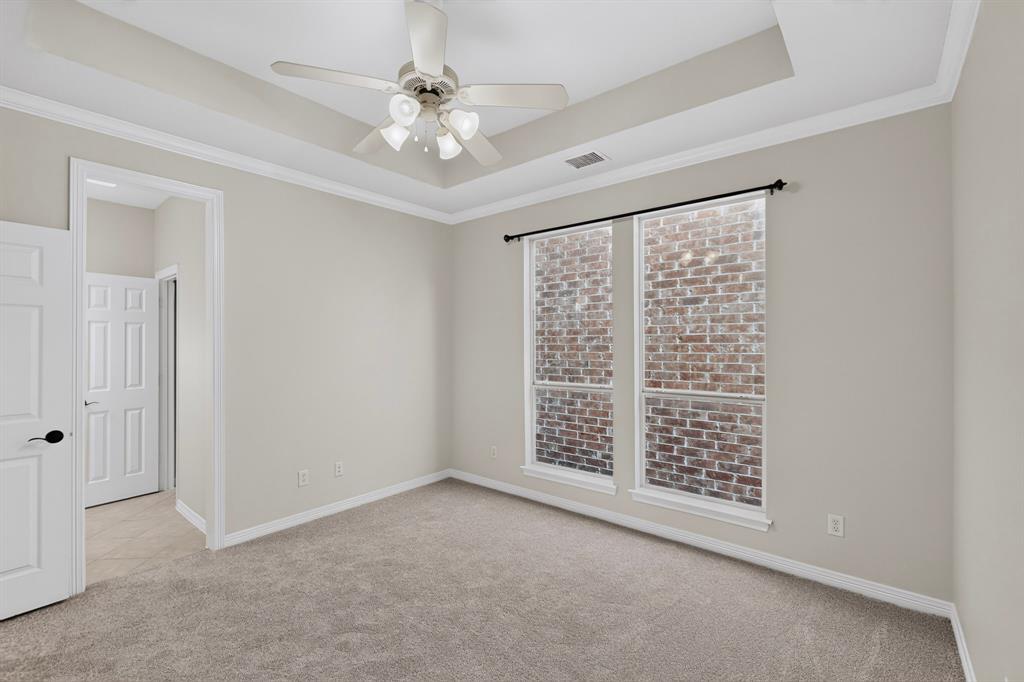 Tray ceiling with a central multi-light ceiling fan, wall-to-wall carpeting, and dual windows with brick exterior detailing