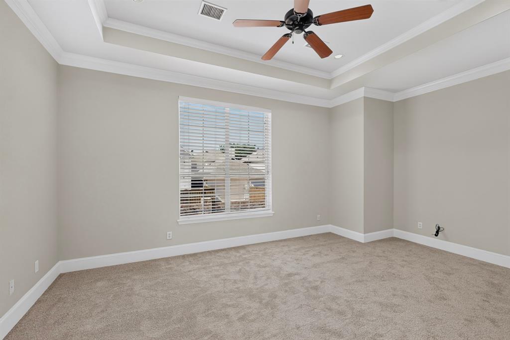 Room featuring a tray ceiling, crown molding, wall-to-wall carpeting, and a ceiling fan