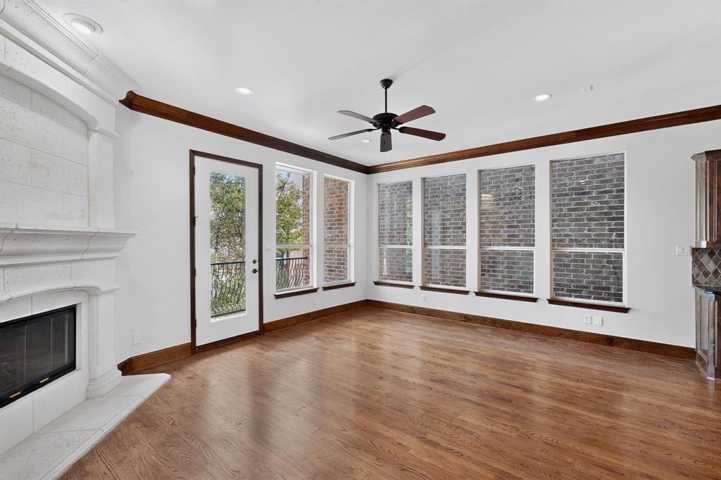 Living area featuring wood-finish flooring, a stone-surround fireplace, extensive brick wall accents, crown molding, and a ceiling fan