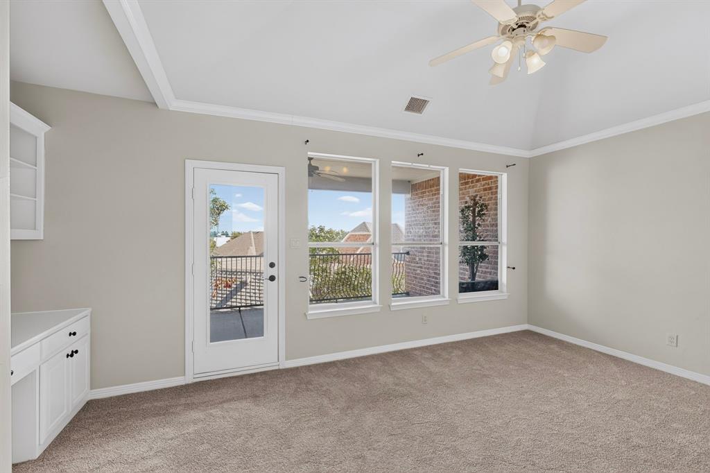 Vaulted ceiling with integrated ceiling fan, built-in cabinetry, carpeted flooring, and glass-paneled door with access to a railed balcony