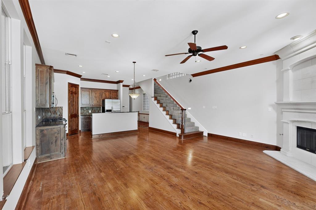 Open-concept area featuring wood-finish flooring, a wood-burning fireplace with an ornate mantel, custom cabinetry, recessed lighting, and a staircase with a metal railing