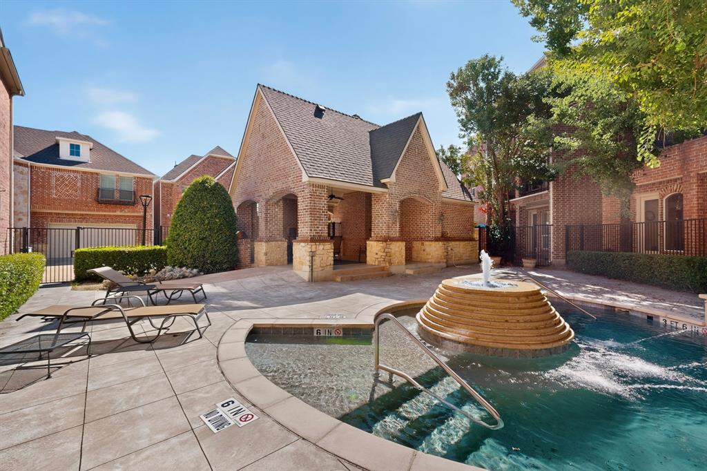 Community swimming pool featuring a stepped stone fountain, paved deck, and a brick-constructed pavilion with stone accents