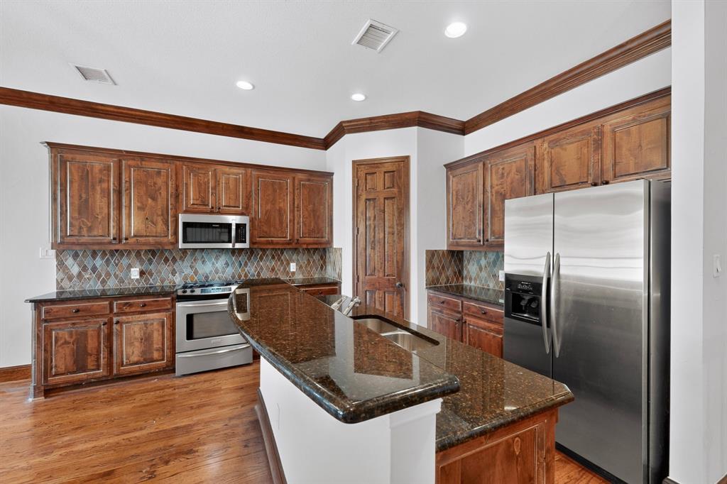Kitchen featuring stained wood cabinetry, stone-finish countertops, diamond-pattern backsplash, stainless steel appliances, and wood-finish flooring