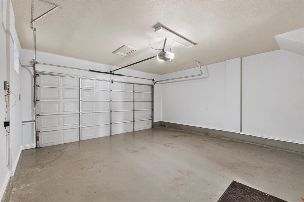 Attached garage featuring a multi-panel overhead door, automated garage door opener, finished walls, and concrete flooring