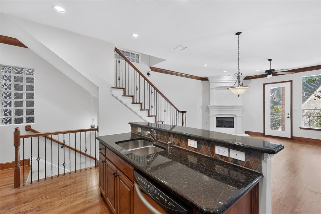 Kitchen featuring a dark stone countertop, undermount stainless steel sink, and wood cabinetry, with an interior staircase accented by decorative metal balusters, glass block accents, and a built-in fireplace