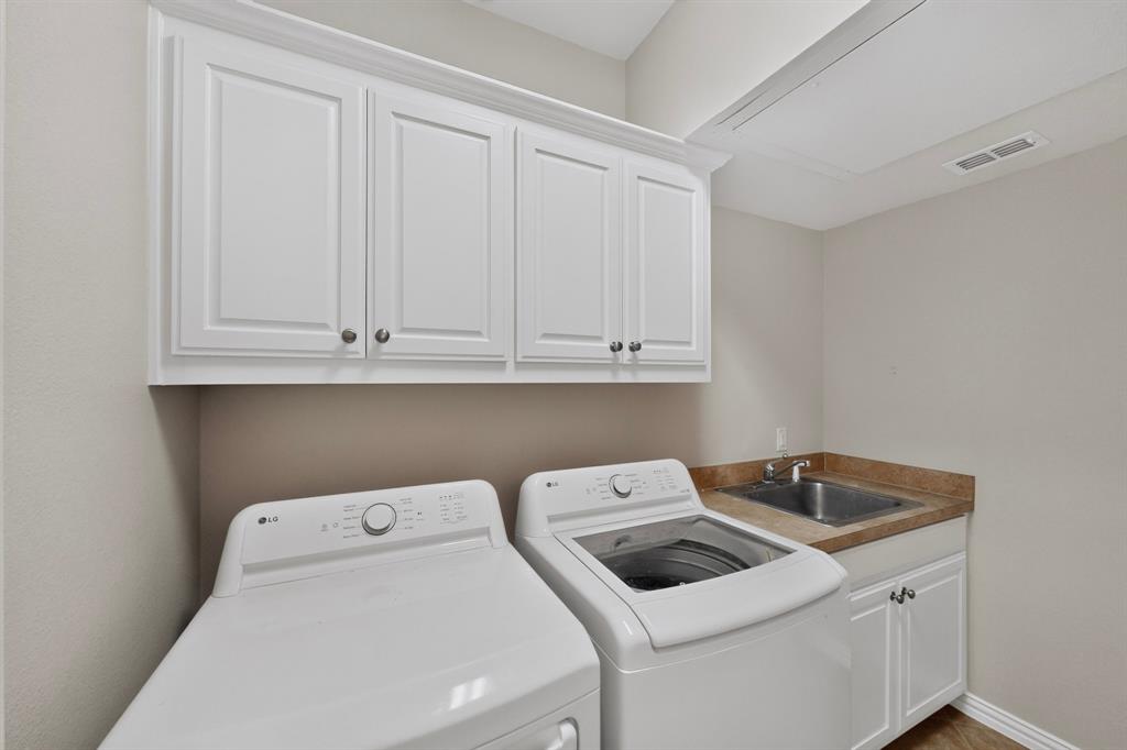 Laundry area featuring white shaker-style wall and base cabinetry, stone-finish countertops, and an integrated stainless steel basin sink