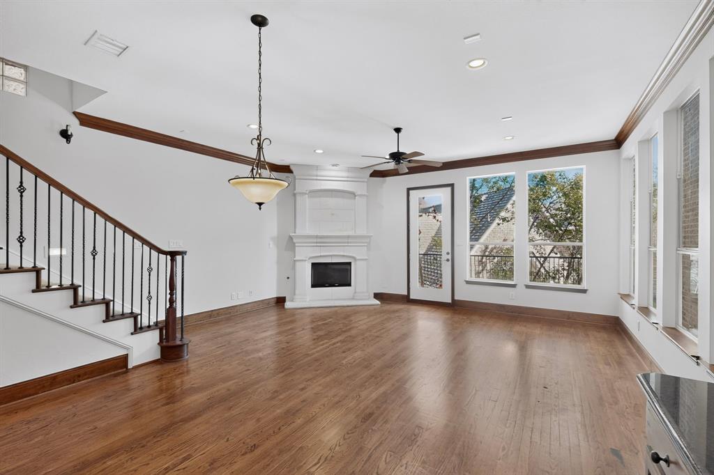 Wood-finish flooring, corner fireplace with a decorative mantel, staircase featuring a wrought-iron balustrade, crown molding, and large windows Wood-finish flooring, corner fireplace with a decorative mantel, staircase featuring a wrought-iron balustrade, crown molding, and large windows