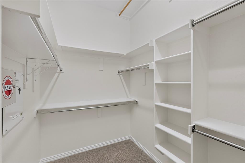 Walk-in closet featuring custom white built-in shelving, multiple tiered hanging rods, and neutral carpeting