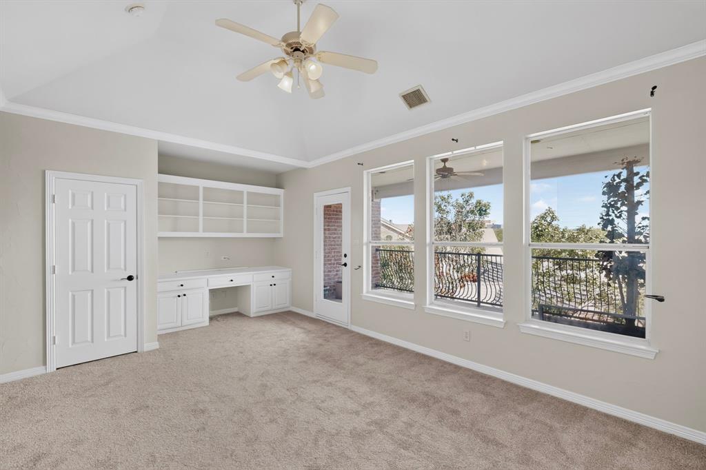 Vaulted ceilings, built-in cabinetry with desk space, ceiling fan with integrated lighting, expansive windows, and access to a wrought-iron railed balcony