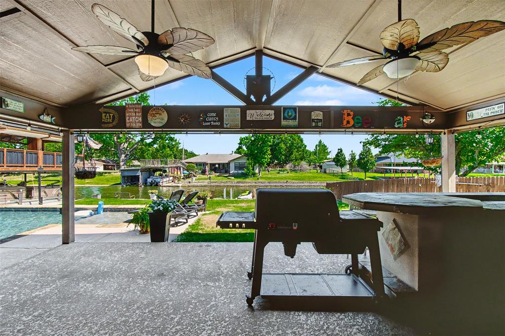 Covered outdoor patio featuring a vaulted ceiling with integrated ceiling fans, a built-in outdoor bar, and concrete flooring
